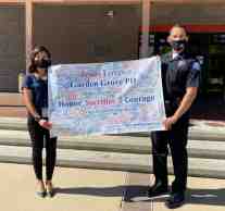 An officer and civilian employee for Garden Grove Police Department hold up banner signed by Calvary Chapel West Grove